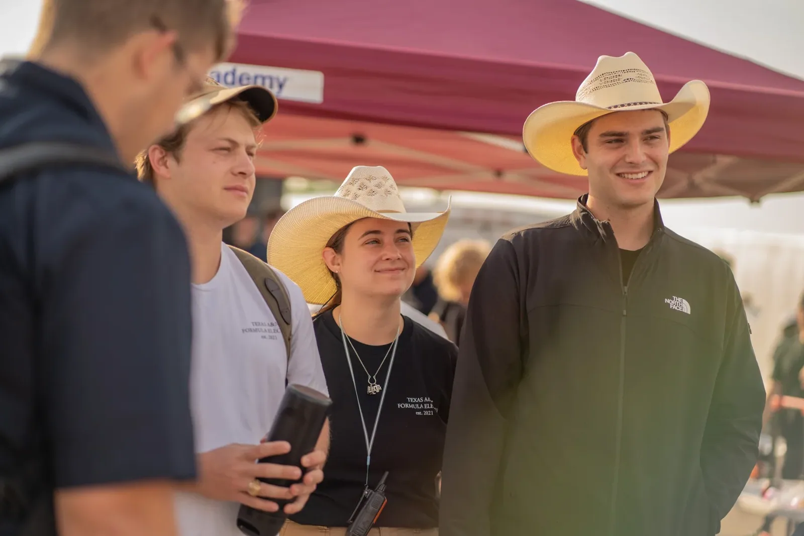 Team members in cowboy hats talking under a tent