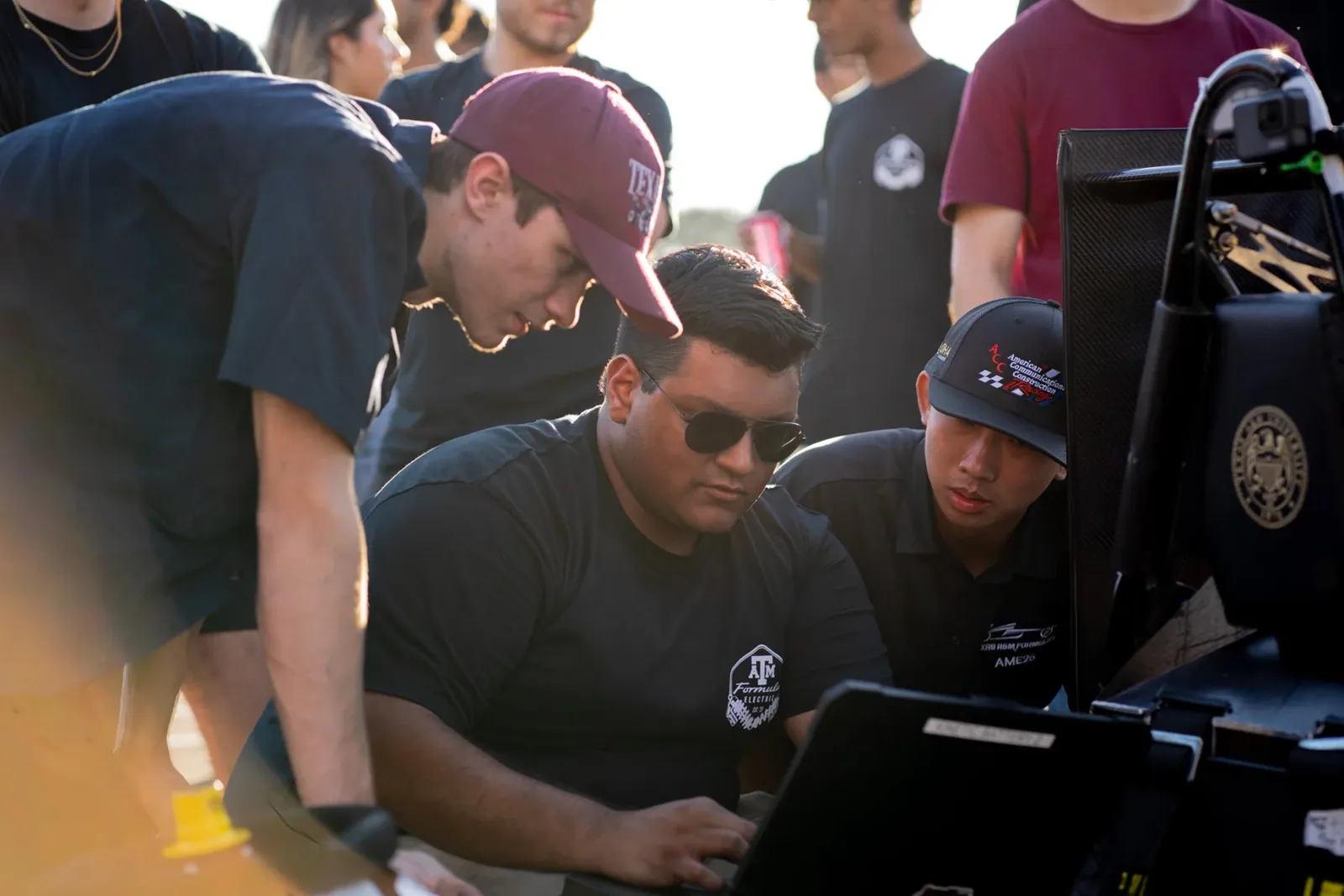 Team members crowded around a laptop beside the car